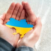 Hands holding national flag of Ukraine in the shape of the borders of Ukraine. Support for Ukraine